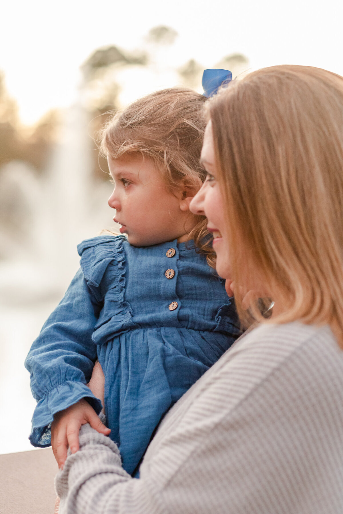 Little girl in blue dress being held by grandmother during outdoor family field session. Image taken by Brandon, Mississippi family photographer.