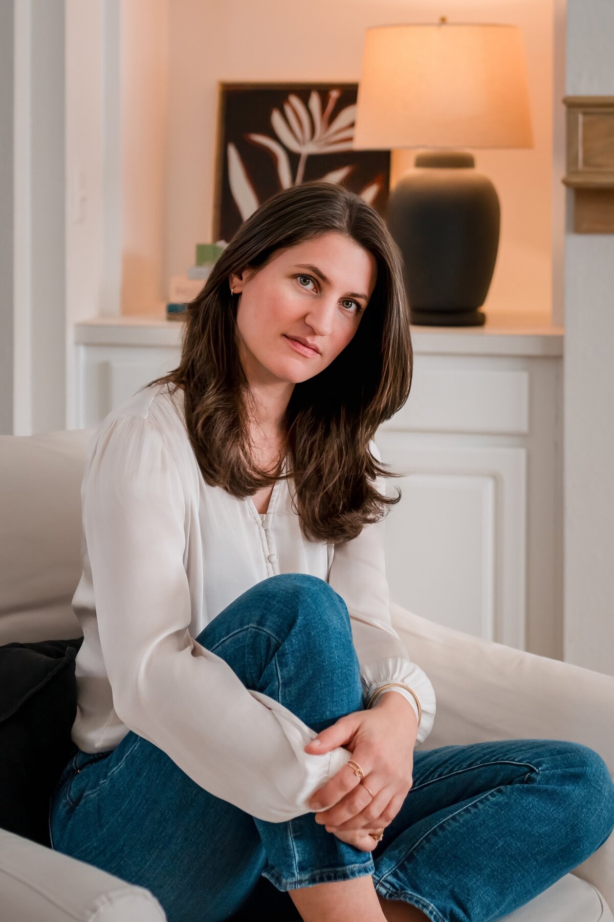 n-home branding photo of Texas artist barefoot in jeans and blouse sitting in cozy living room."
