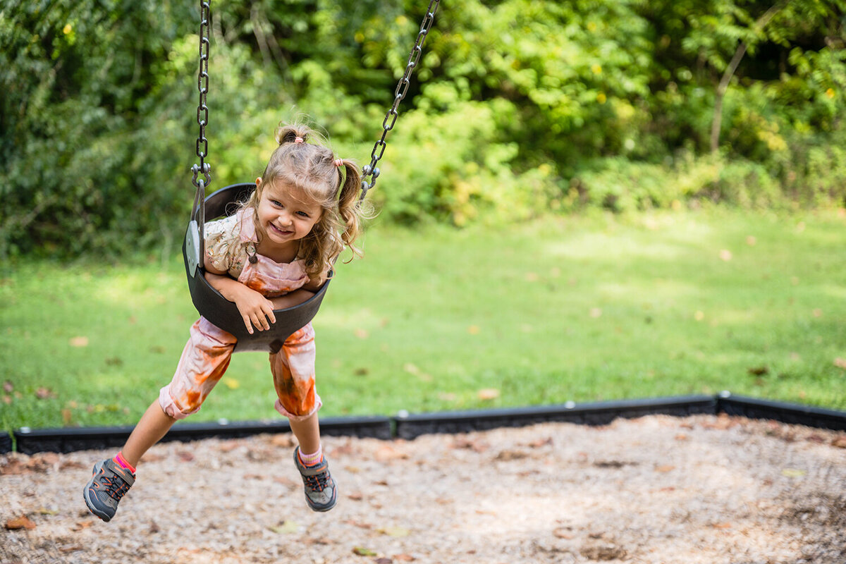 A child in a swing smiles gleefully as she’s pushed into the air at Fishburn Park in Roanoke, Virginia.