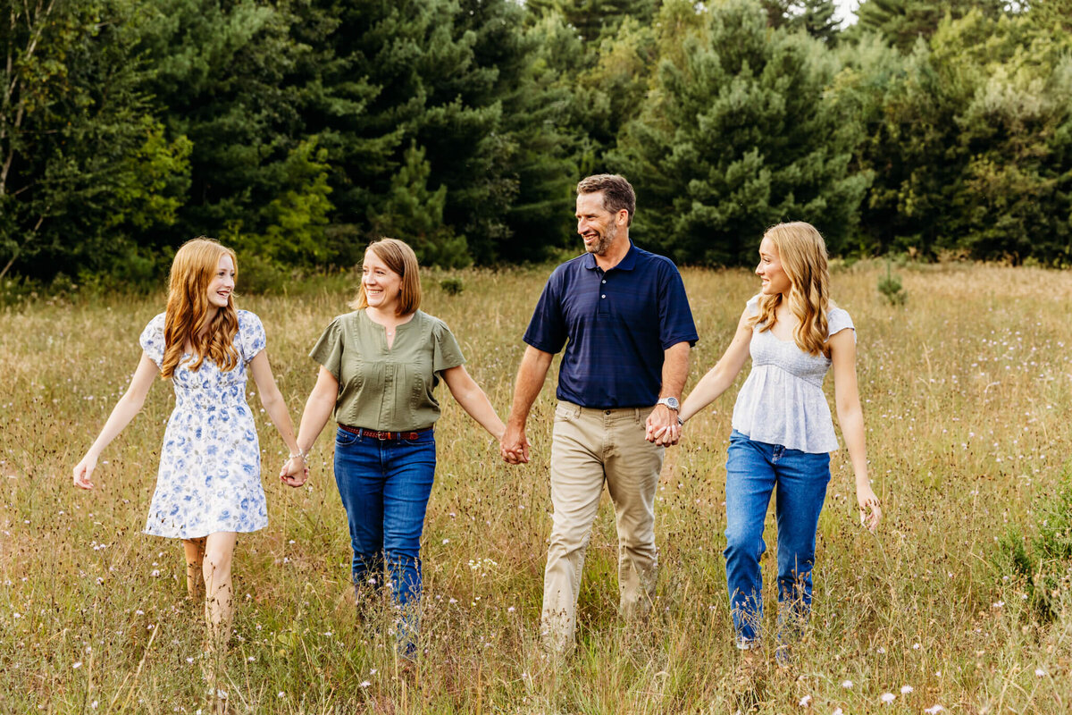 mom and dad walking with their two teenage daughters in a beautiful field captured by Ashley Kalbus