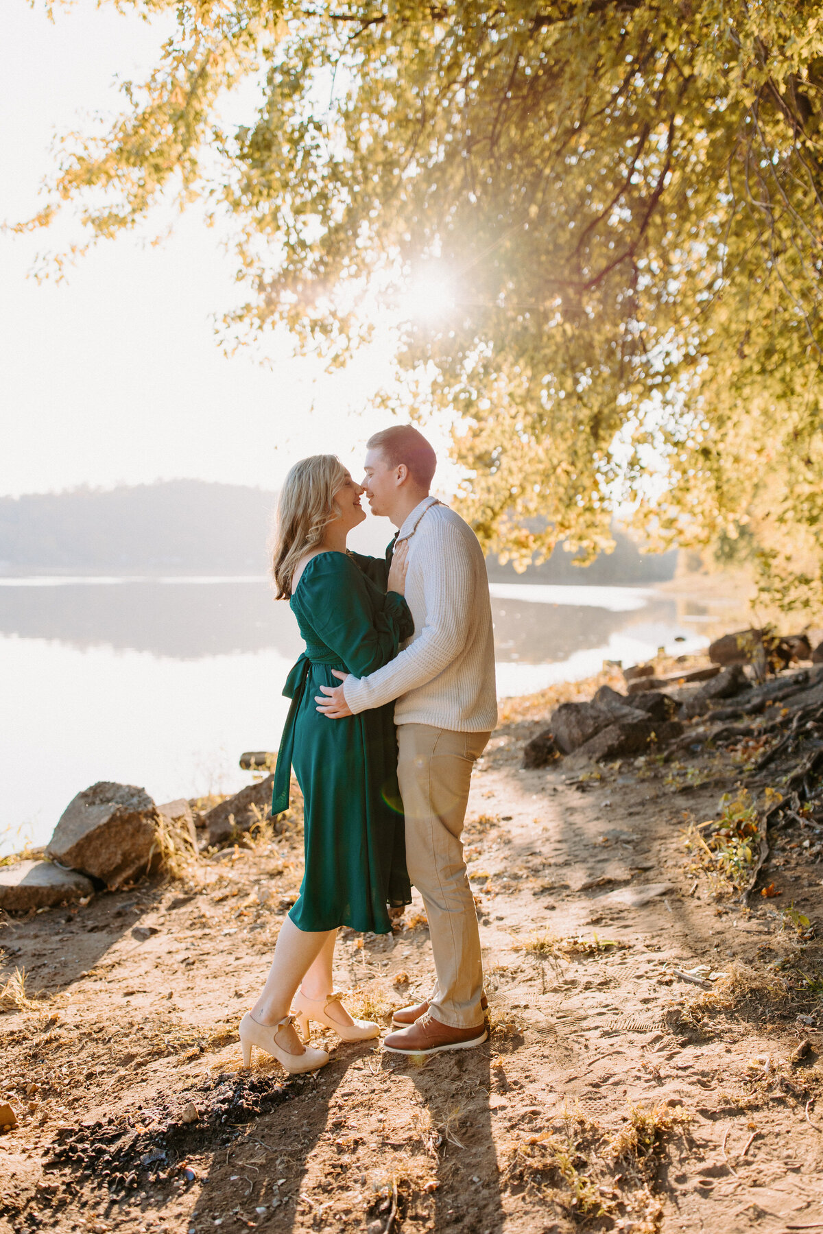 couple with their arms around each other about to kiss next to a lake