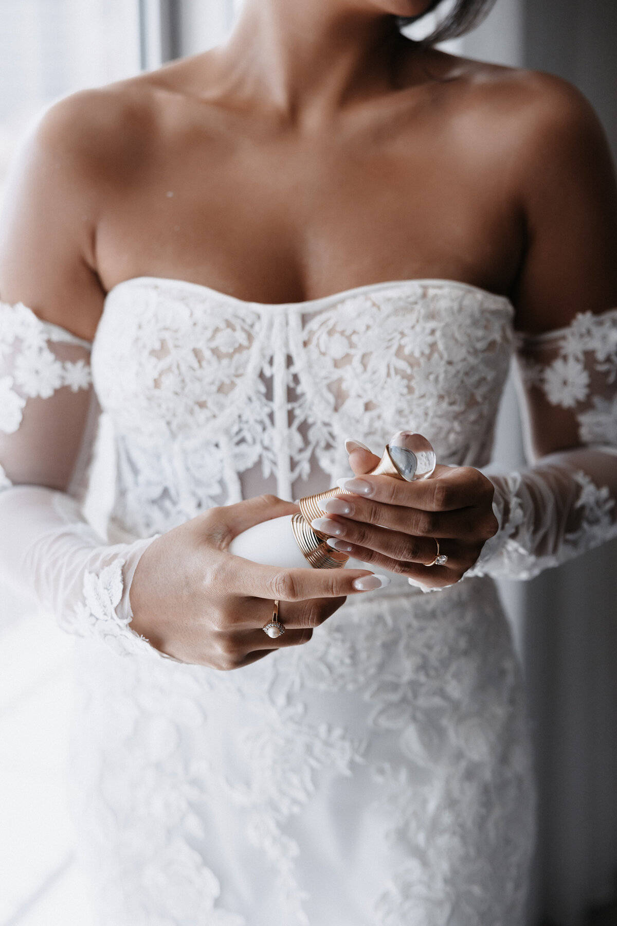 Bride in lace strapless wedding dress and detacehd long sleeves holding perfume