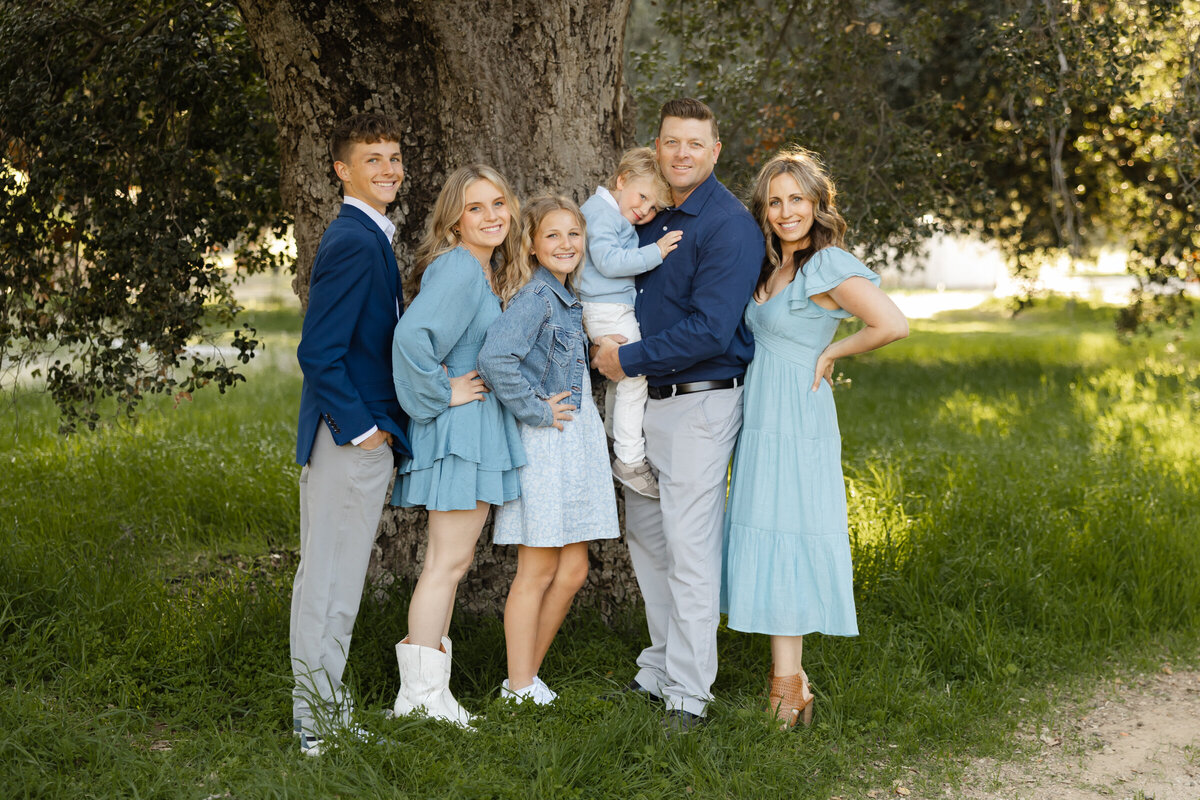 Family of five smiling together outdoors, wearing coordinated blue outfits. Photographed by Yucaipa family photographer Kaitlyn Dawn Photography.