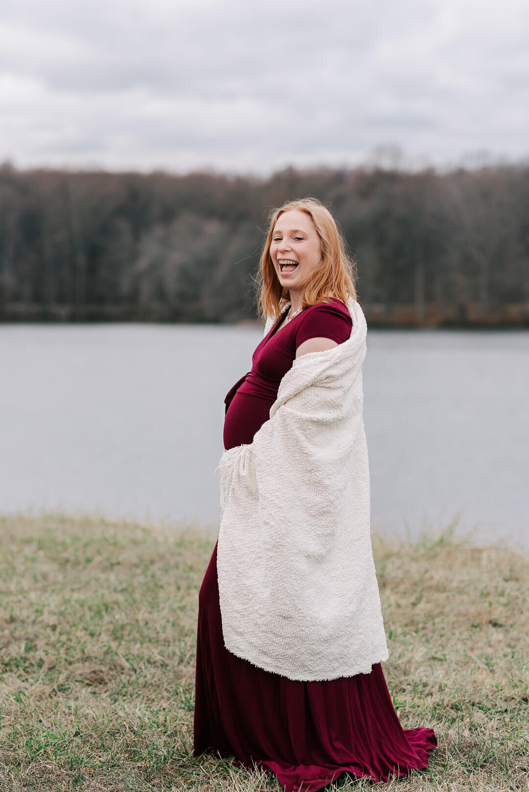 A red-headed pregnant woman holding a warm blanket joyfully laughing during her maternity session
