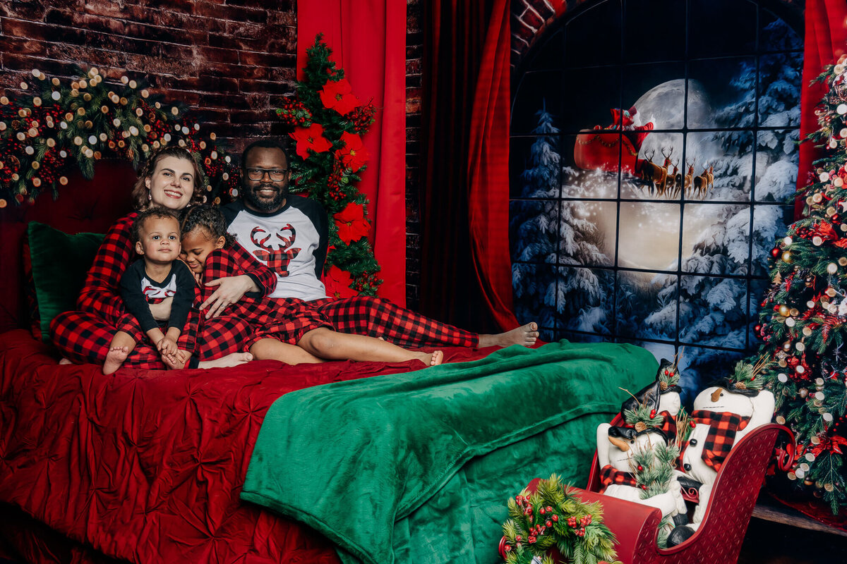 Family poses on bed with Santa out the window in  holiday session with Prescott family photographer Melissa Byrne