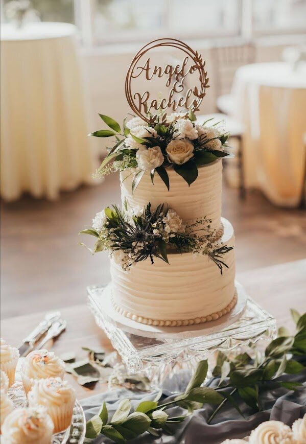 A whited textured wedding cake on a clear stand with fresh flowers filling the top and a cluster on the side.