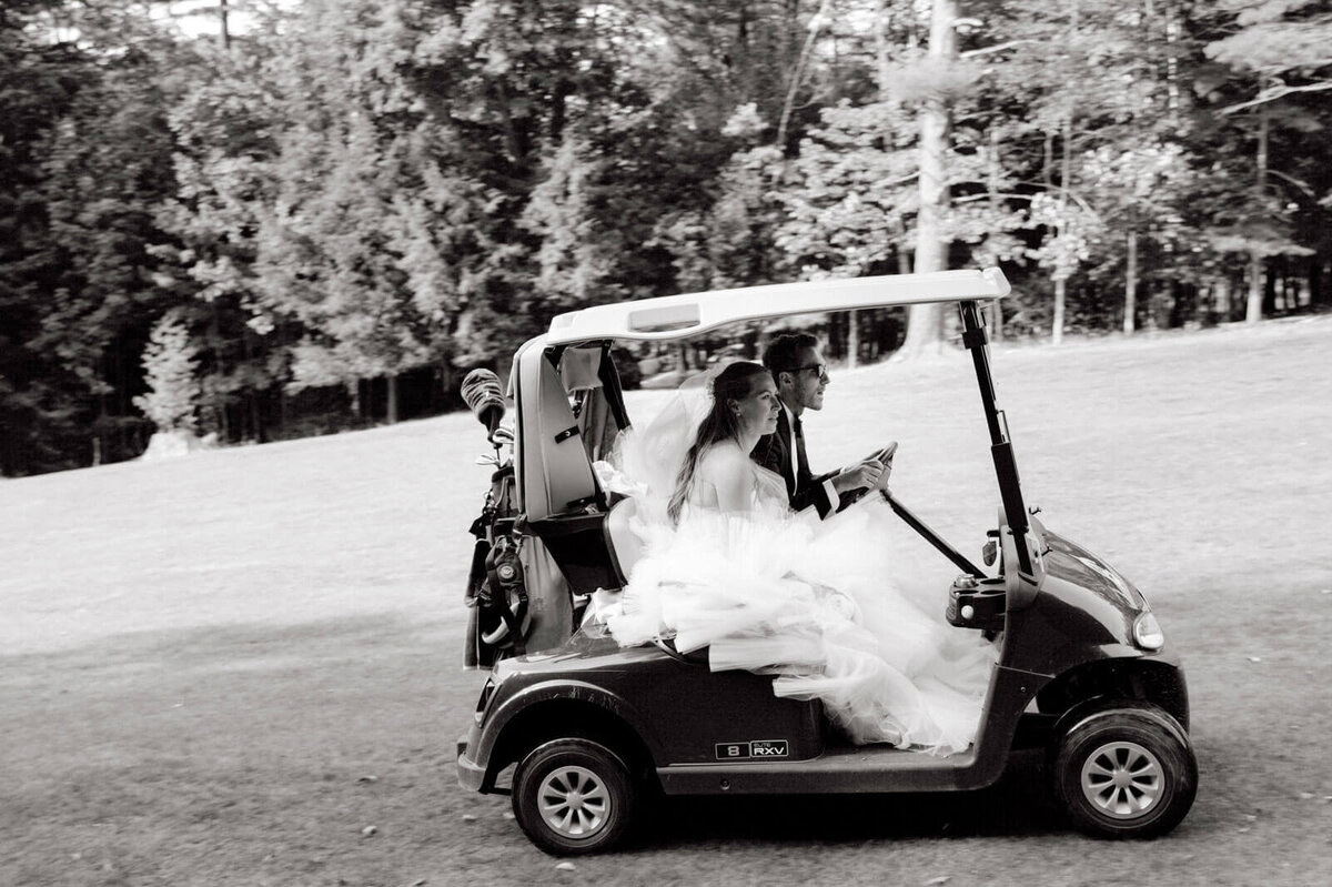 Black and white photo of the bride and the groom riding a golf cart at The Ausable Club, NY. Image by Jenny Fu Studio.