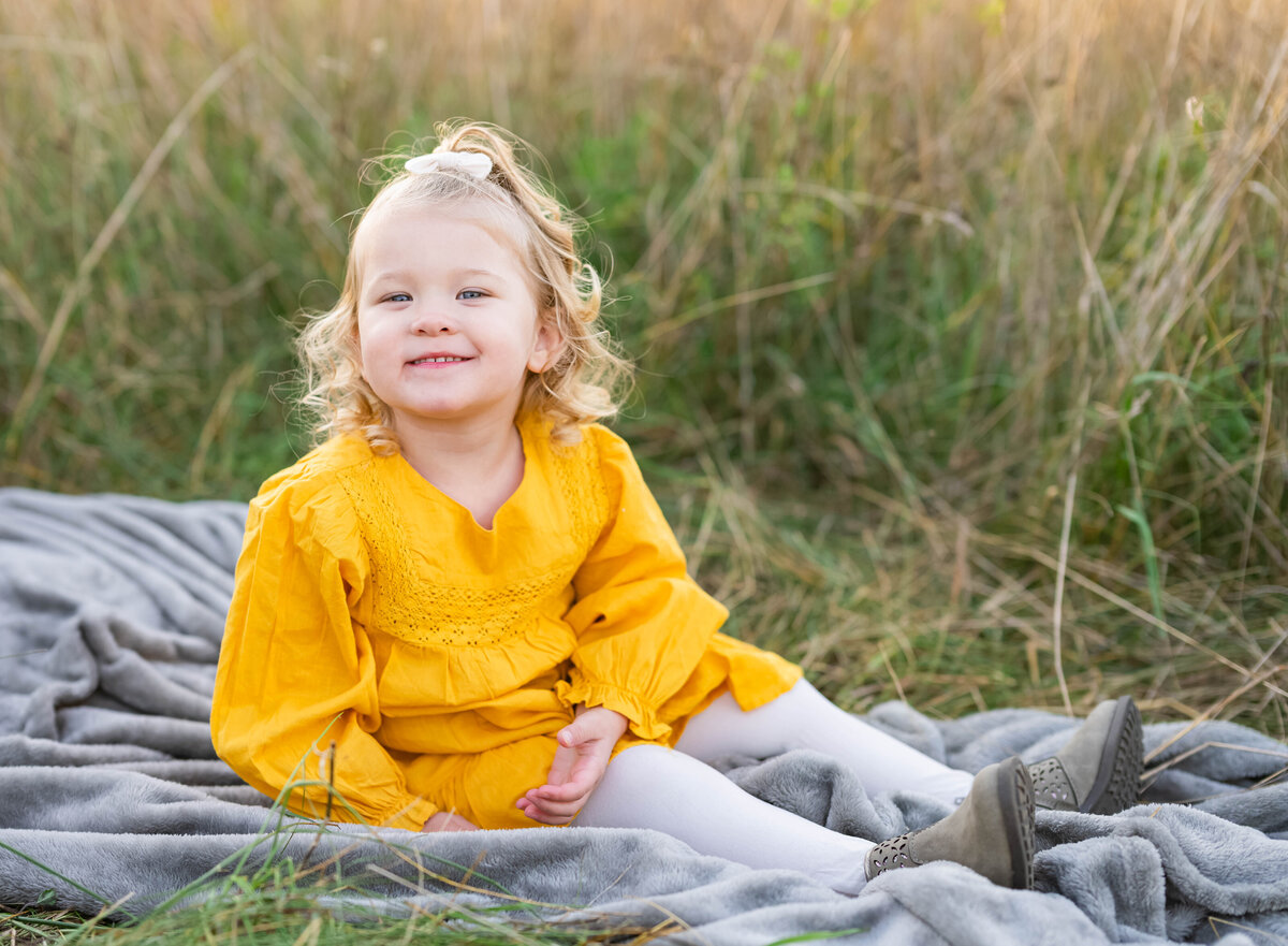 young girl sitting on blanket in field