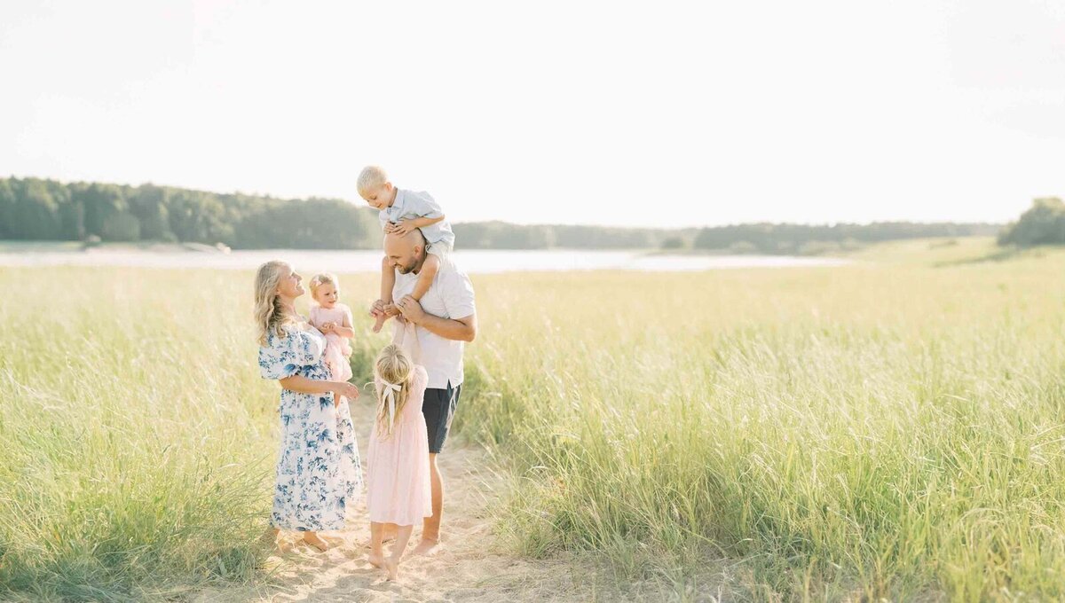 Family of Five on a private beach in Maine.  The father has the little boy on his shoulders while mom holds the littlest one.  The Older Daughter is playing and tickling her brothers feet.  This coastal family session was captured by Maine Photographer, Carrie Pellerin.
