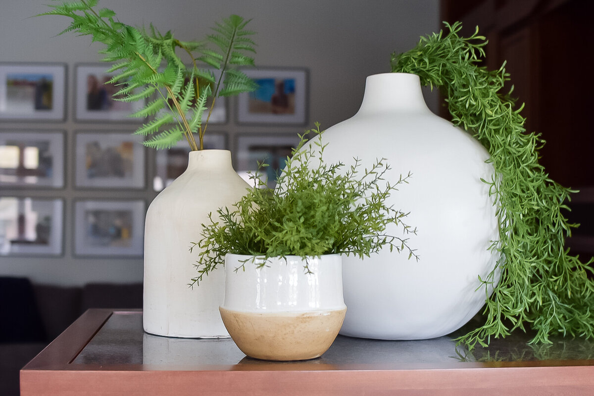 Three white vases with draping greenery sit on a fireplace mantle