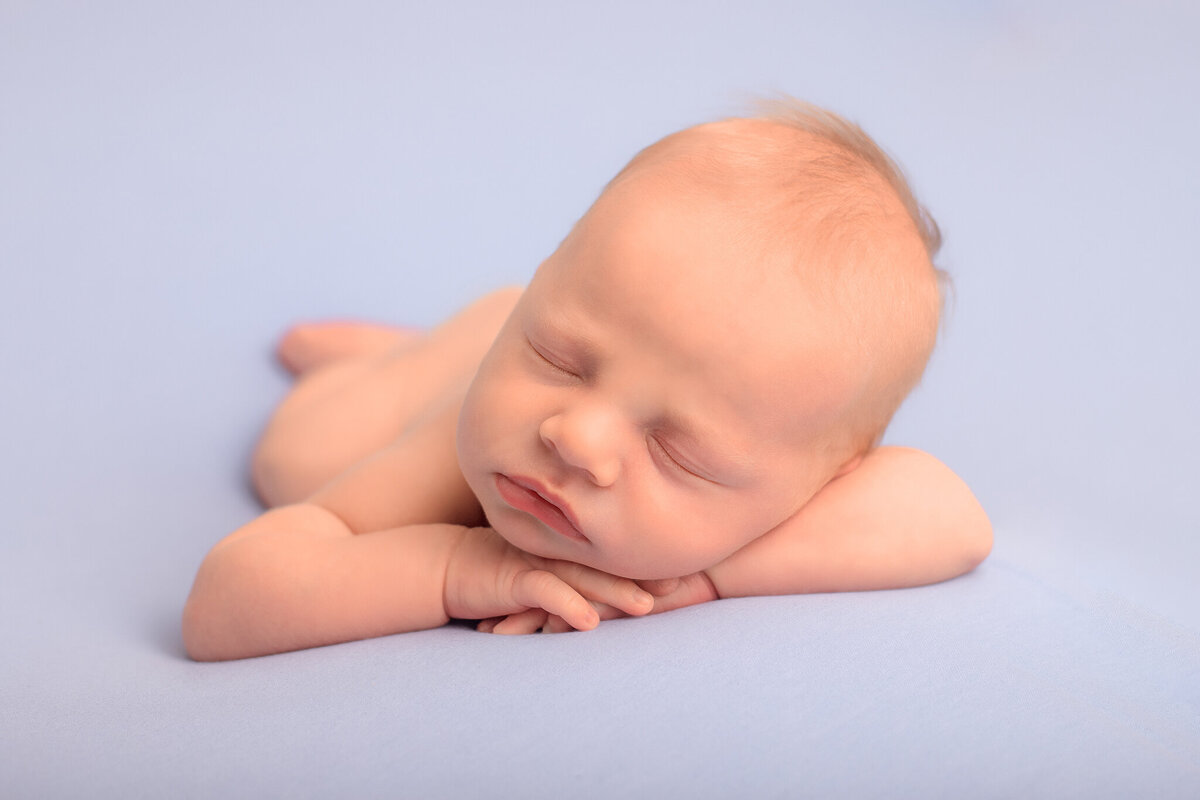 Nyfödd bebis i chin on hands pose med blå bakgrund