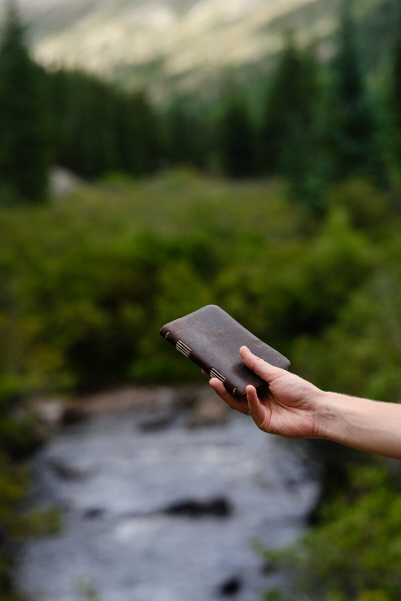 A denver commercial photographer and product photographer in denver takes an outdoor picture of a journal in a beautiful Colorado setting with a river in the background to be used for denver brand pictures and branding photos for an etsy shop for leather goods and leather journals.