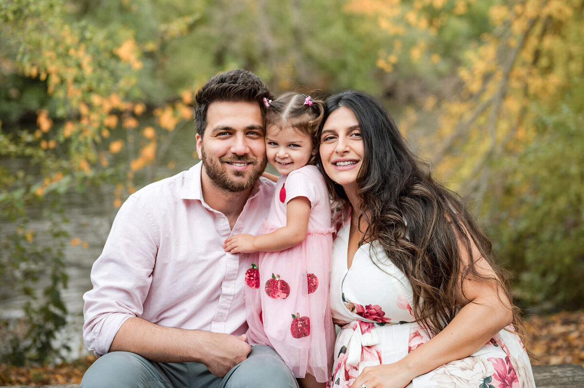 Family standing in fall foliage posing for maternity photos at Island Park in Ann Arbor