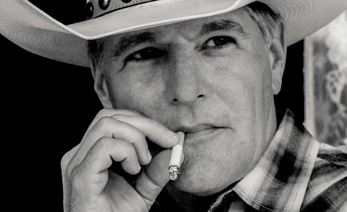 Country musician portrait Darrell Goldman black and white close up smoking cigarette wearing plaid shirt with white cowboy hat