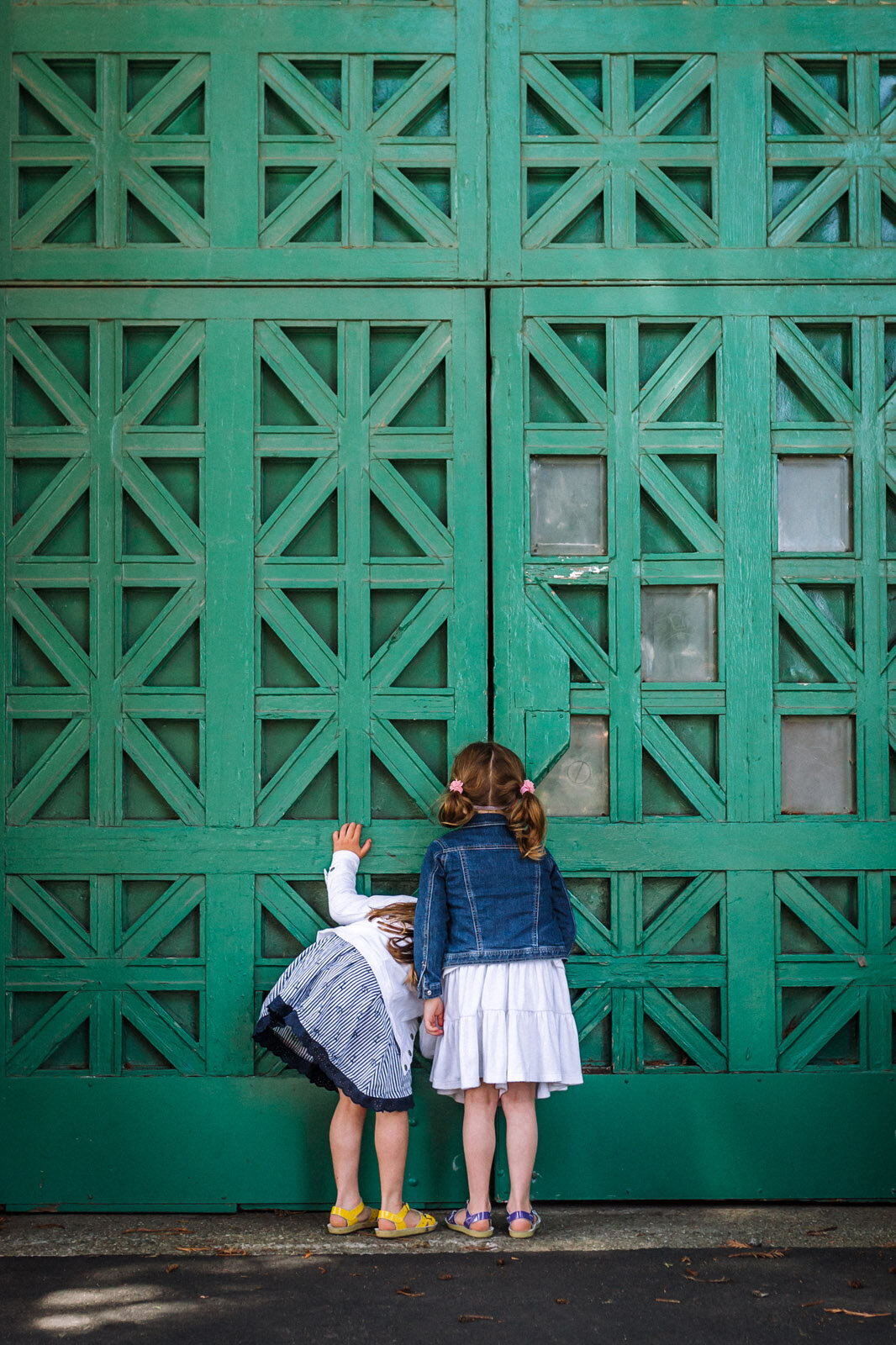 back of two girls in skirts and sandals trying to peer in crack of green doors in San Francisco