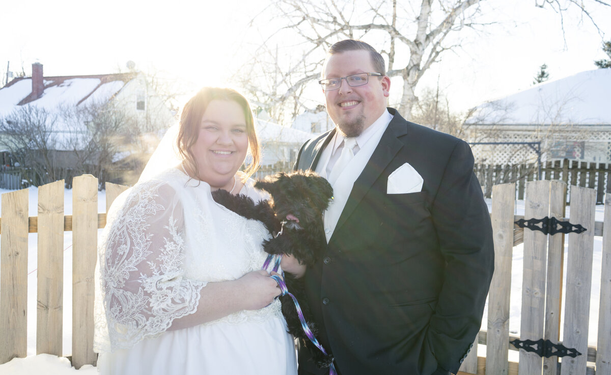 Photo of a bride and groom holding their dog and smiling