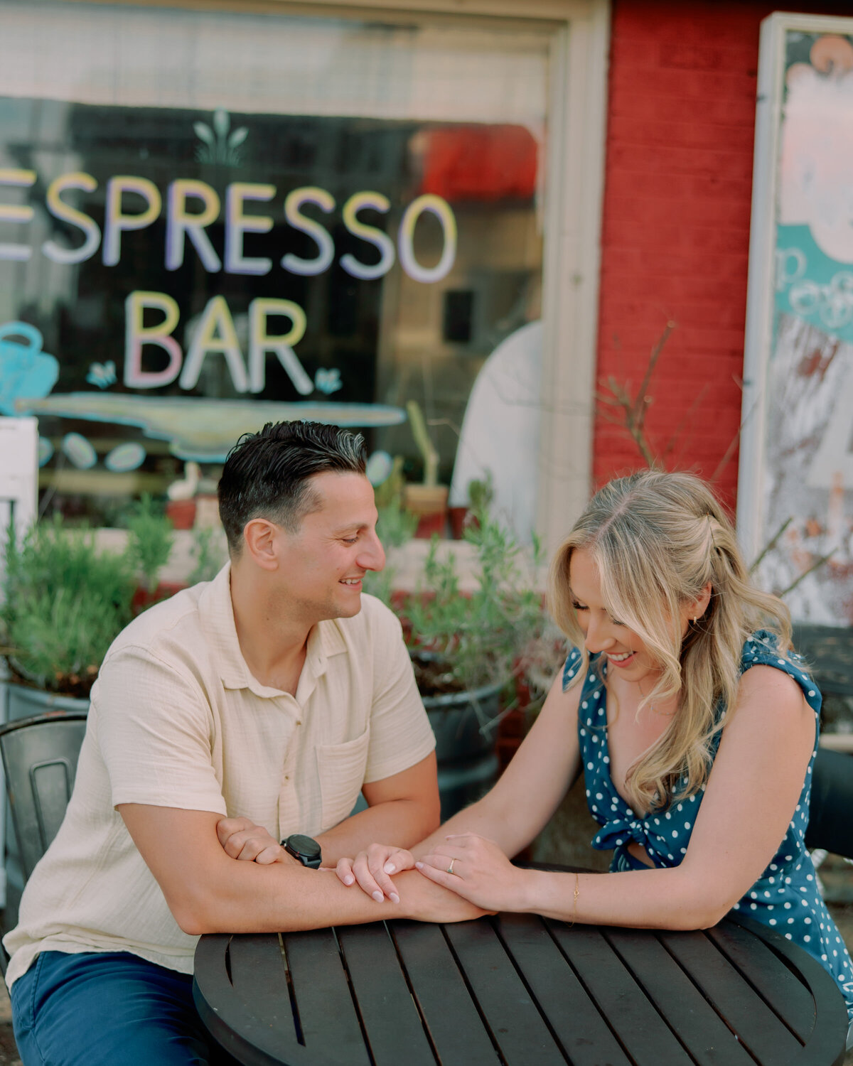 A couple sitting at a small outdoor cafe table holding hands 
