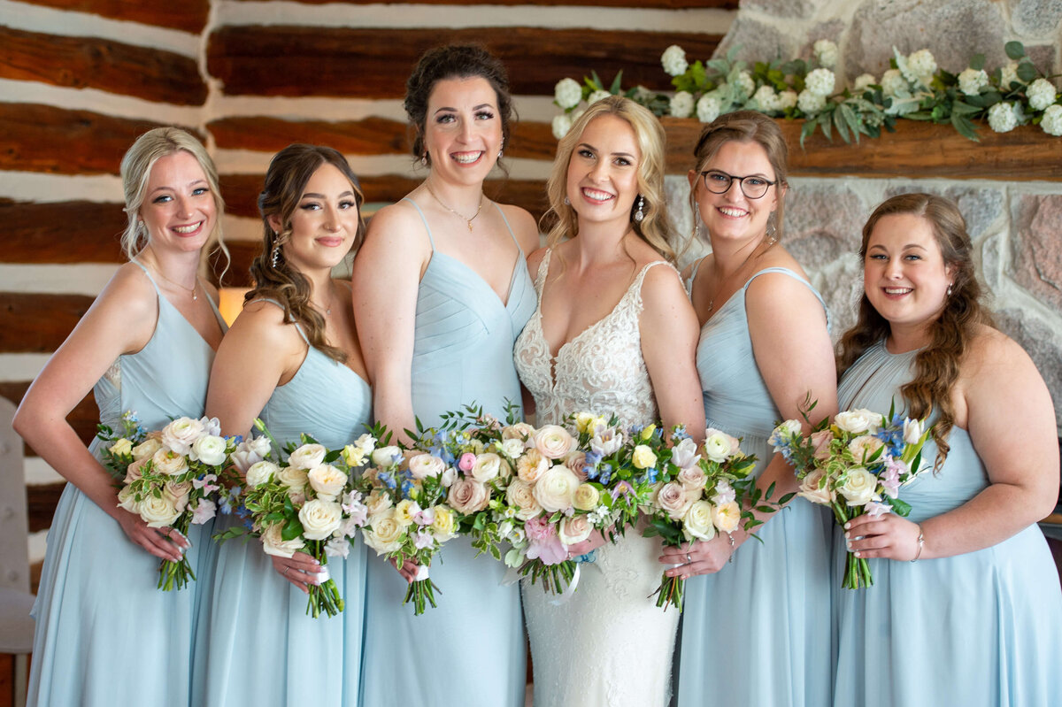 smiling bride and bridesmaids dressed in blue gowns getting ready in the Farmhouse at Stonefiields Estate wedding venue.  Captured by Ottawa wedding photographer JEMMAN Photography