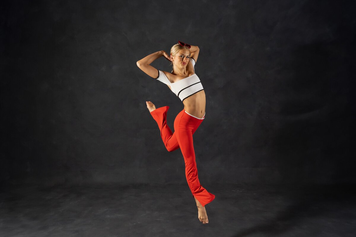 Professional lifestyle portrait of dancer in white crop top and red pants captured by St Augustine lifestyle photographer against dark backdrop