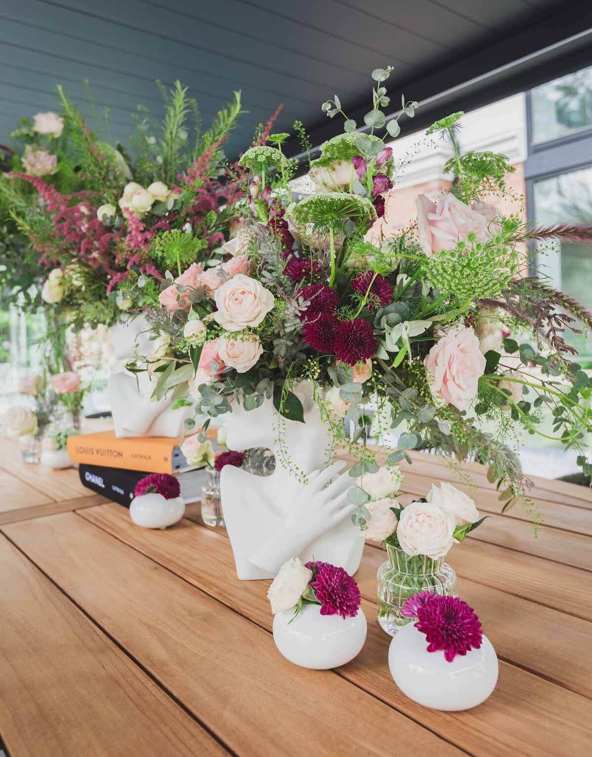 Flower arrangements in a white vase with small flowers sat on a wood table