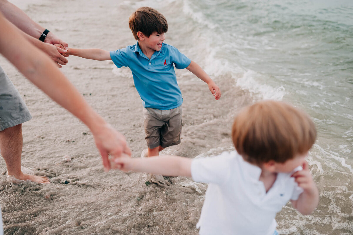 parents hold their son's hands as the boys try to run into the water during their photoshoot with boston family photographer, Allison Wolf