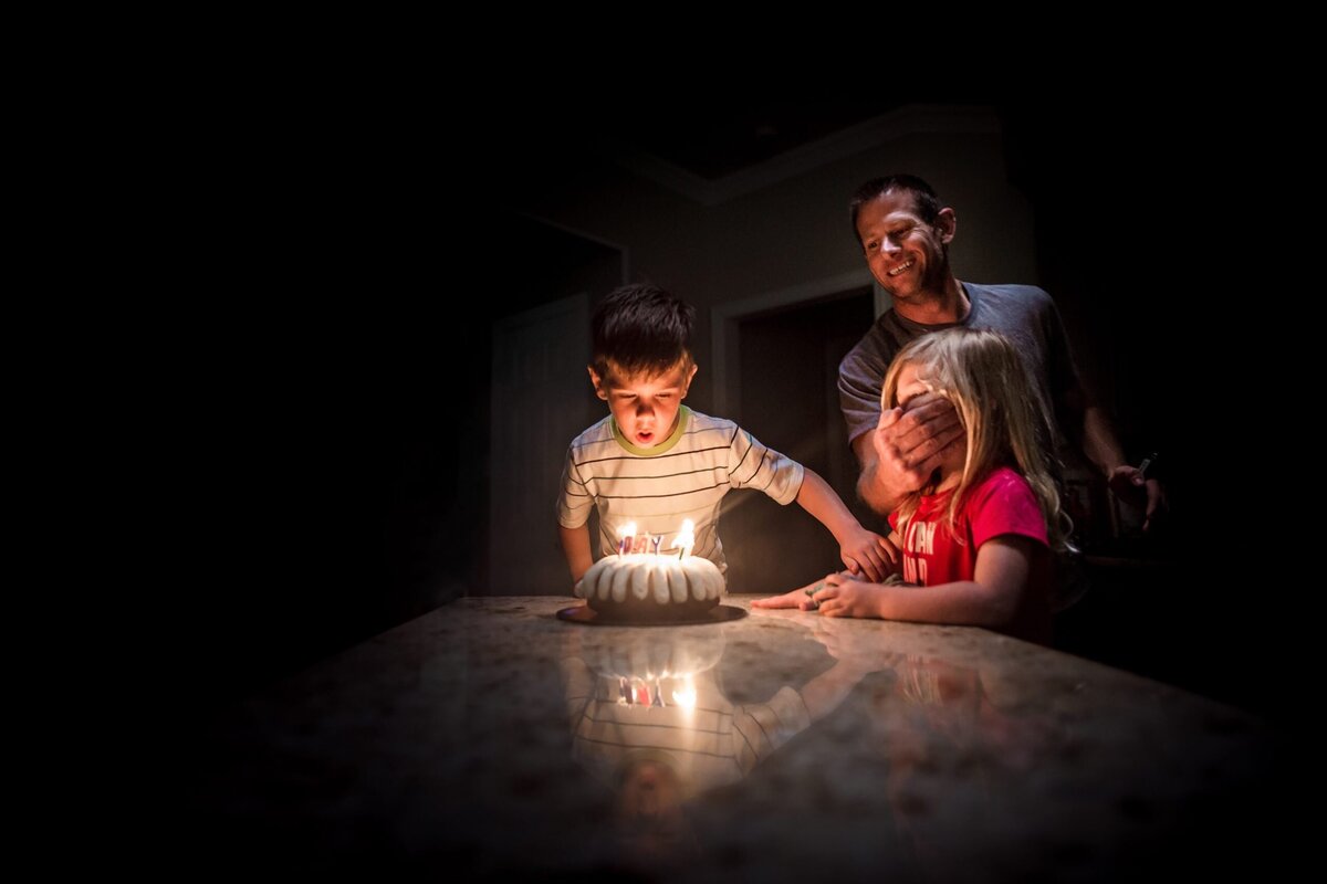 A young boy blows out his birthday candles while trying to stop his sister from blowing them out.