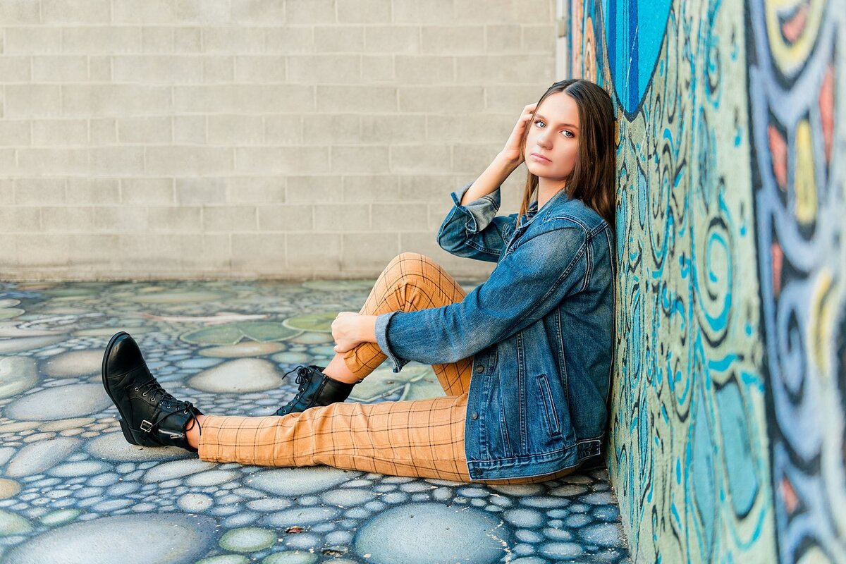 High school senior girl sitting leaning on graffiti wall