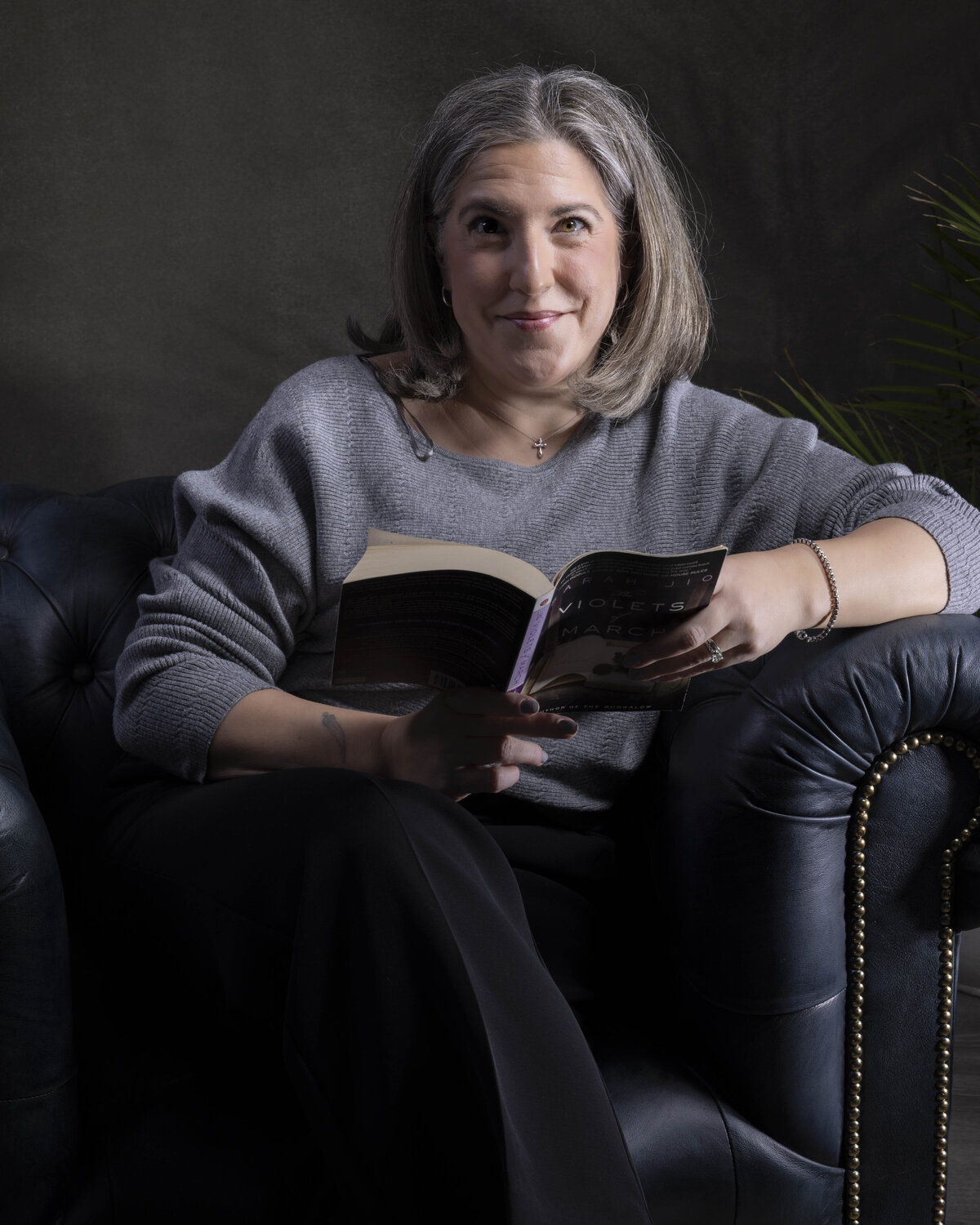 Professional headshot in MA of woman reading in leather chair, casual and approachable, by Rob Faber Photography.