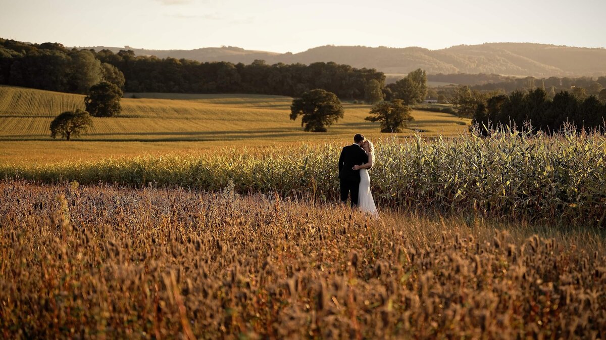 Bride and groom embracing while surrounded by beautiful countryside with golden hues.