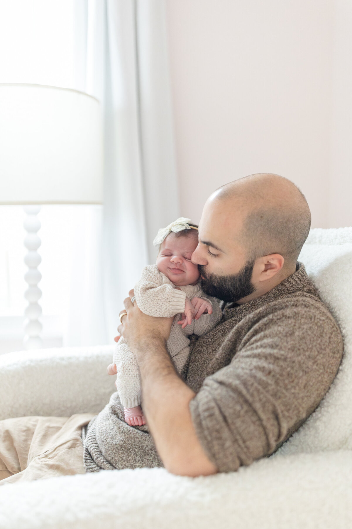 Dad snuggles his newborn while sitting on the couch in their home during a session with Oak and Lore Studios. He holds the baby close, capturing a tender and intimate moment filled with love and warmth