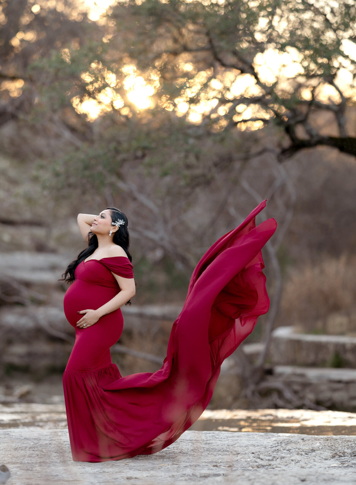 Dramatic outdoor maternity photo with flowing red gown and sunset backlight in Austin, Texas