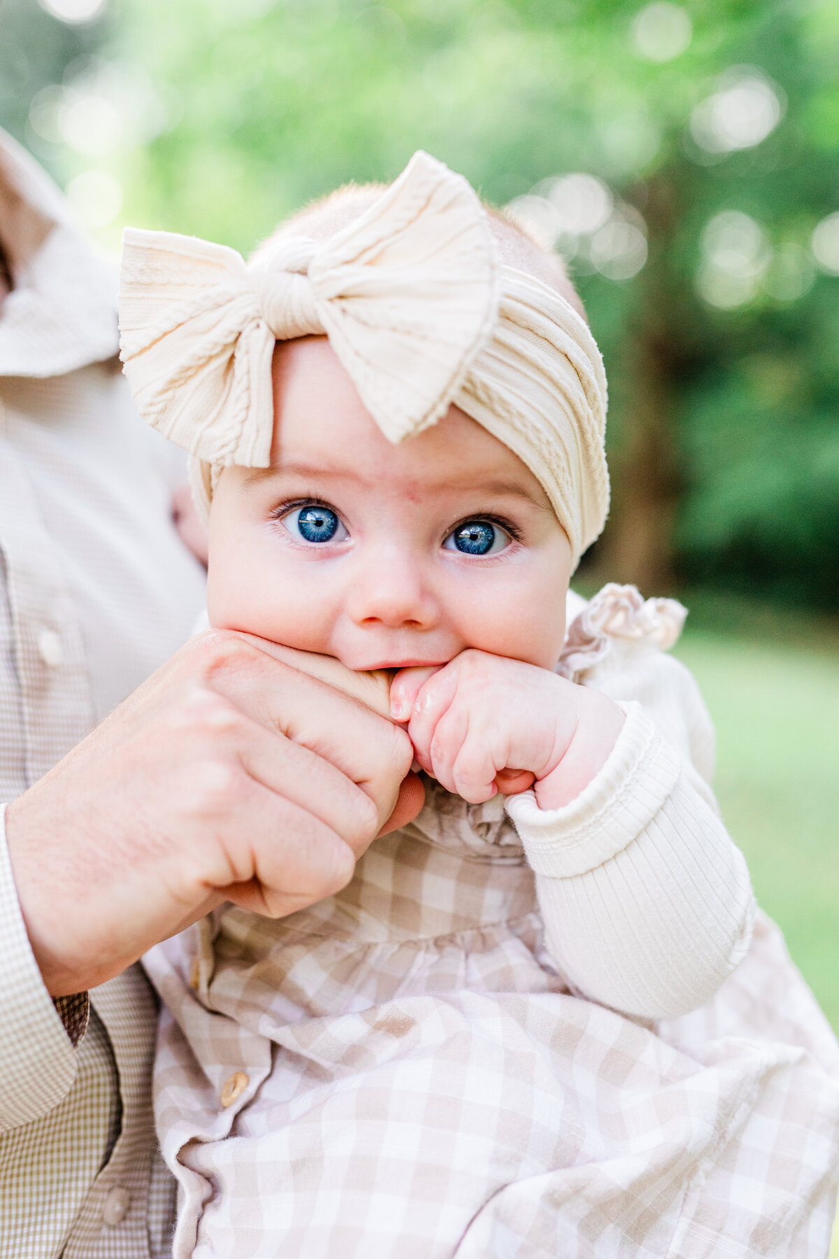 Six month old baby girl biting her dad's finger with bright blue eyes and a bow