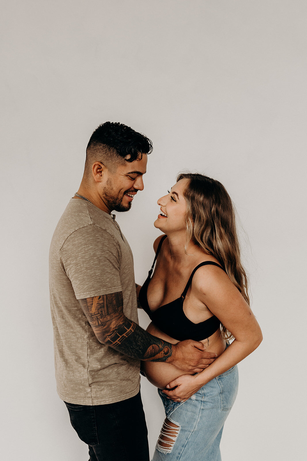 pregnant wife laughs while husband holds her close
