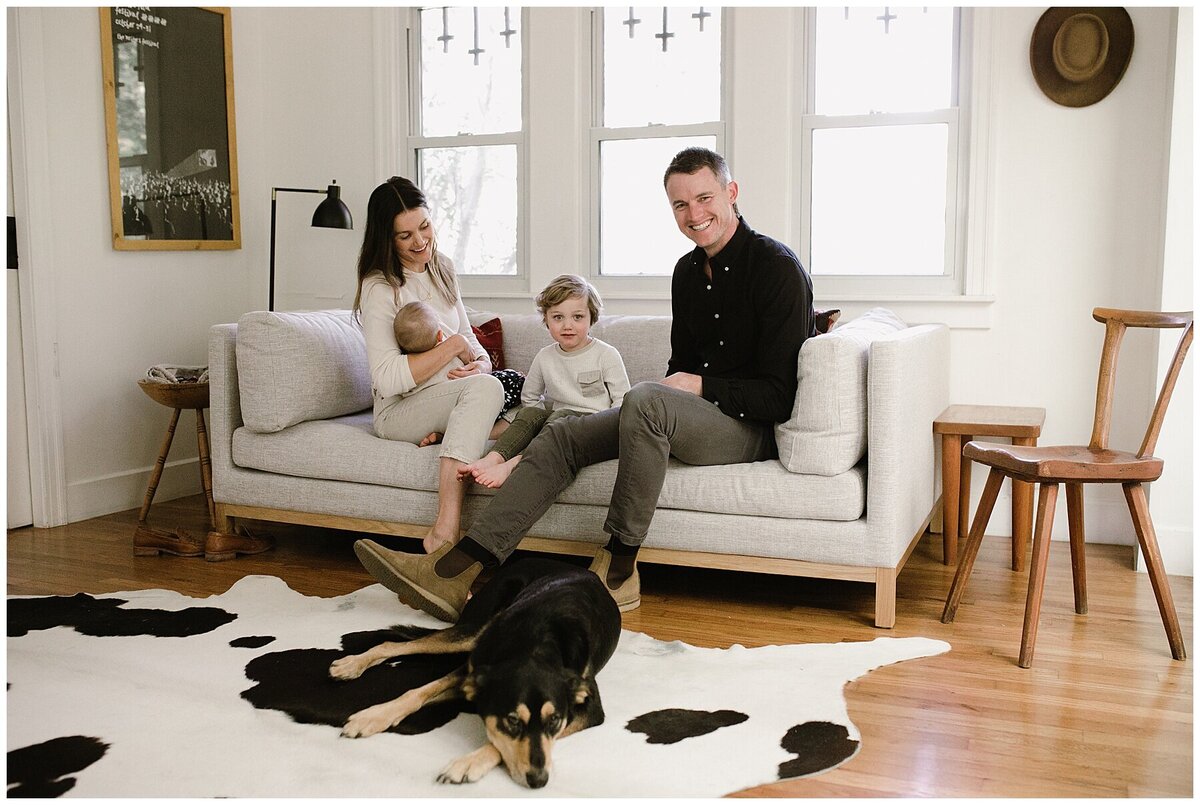 Family with baby and toddler sitting on sofa with dog laying on rug at  sweet at home family session in Austin by Amber Vickery Photography