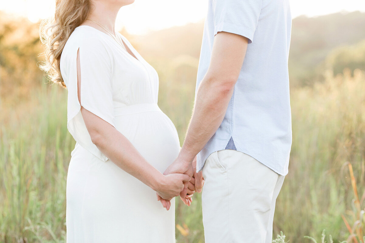 Pregnant couple hold hands at Louisville KY Parklands field during maternity photo shoot with Julie Brock Photography