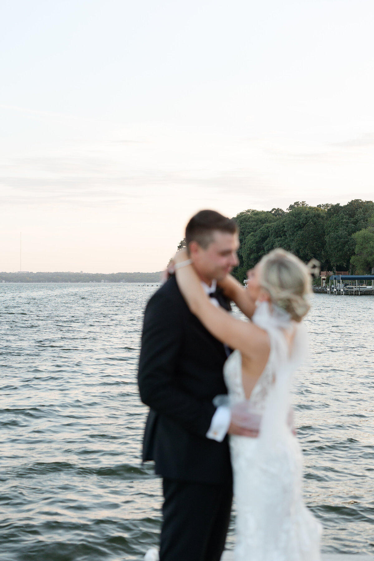 Bride and groom embracing during golden hour at Bishops Bay Country Club, with Lake Mendota's serene waters in the background.