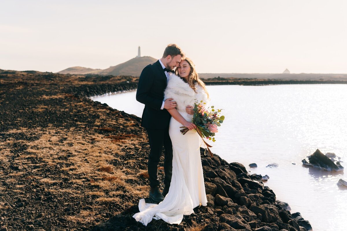 In this enchanting portrait, the couple snuggles close, their love nearly blossoming into a kiss. The Blue Lagoon graces one side, while a distant lighthouse adds a touch of charm to this captivating moment.