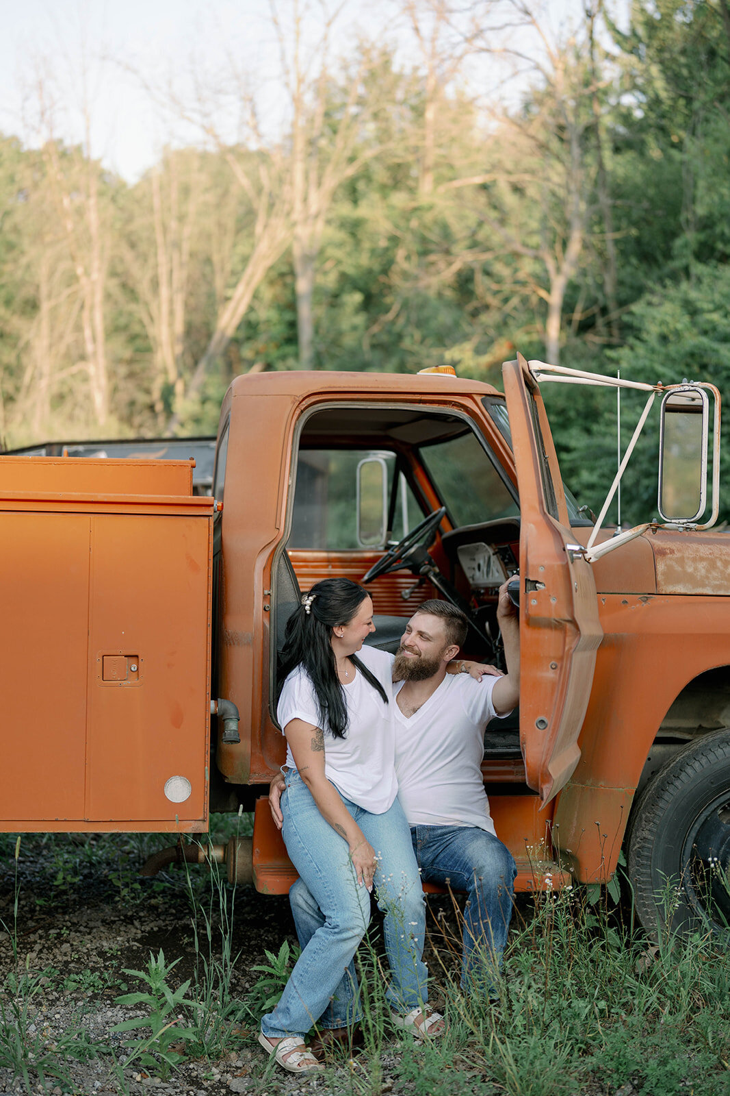Kali and Joe smiling and standing close beside a vintage orange truck during their Detroit engagement photos.