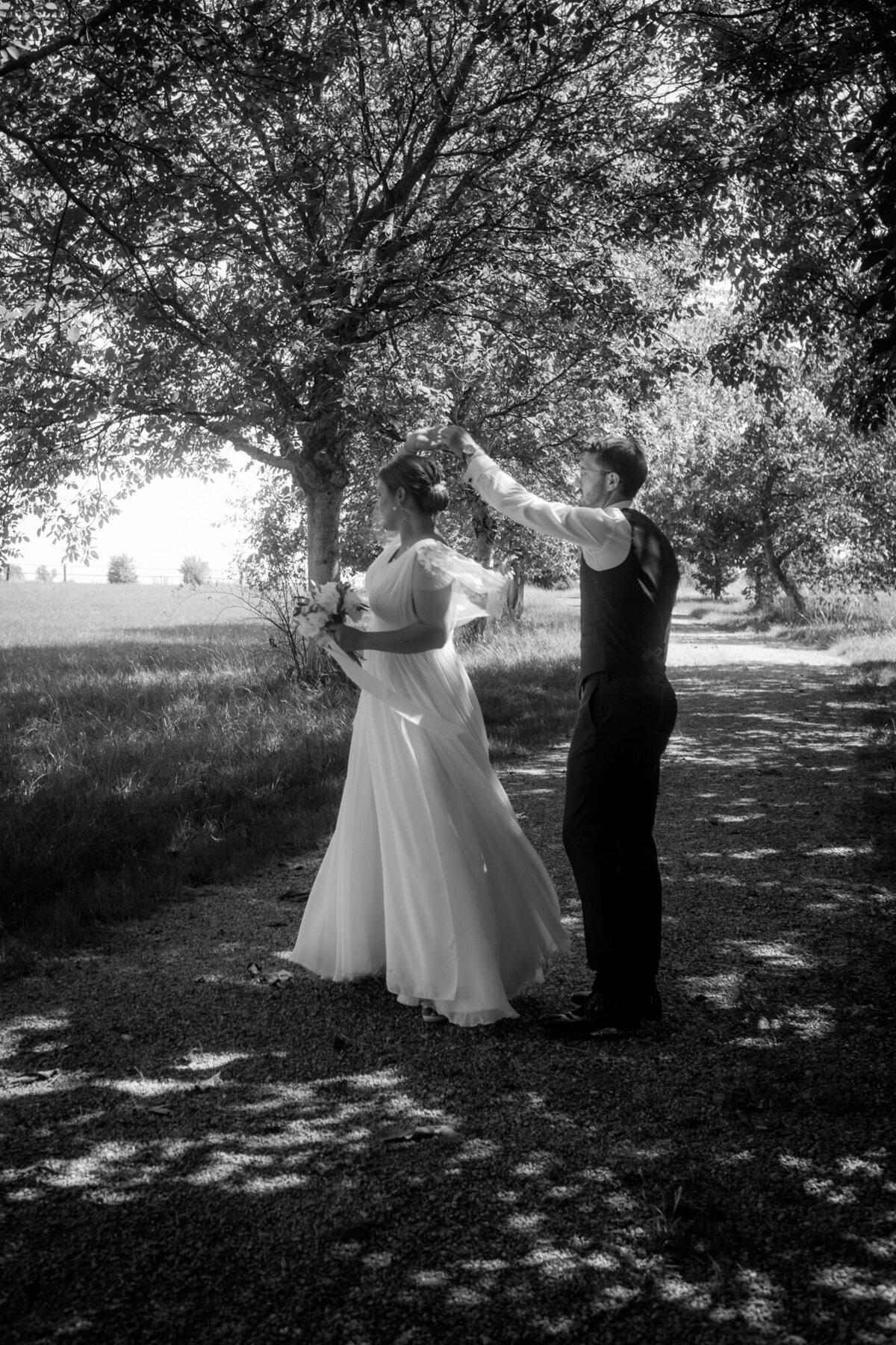 Das Hochzeitspaar tanzt auf einem Feldweg. Der Bräutigam dreht seine Braut im Kreis.