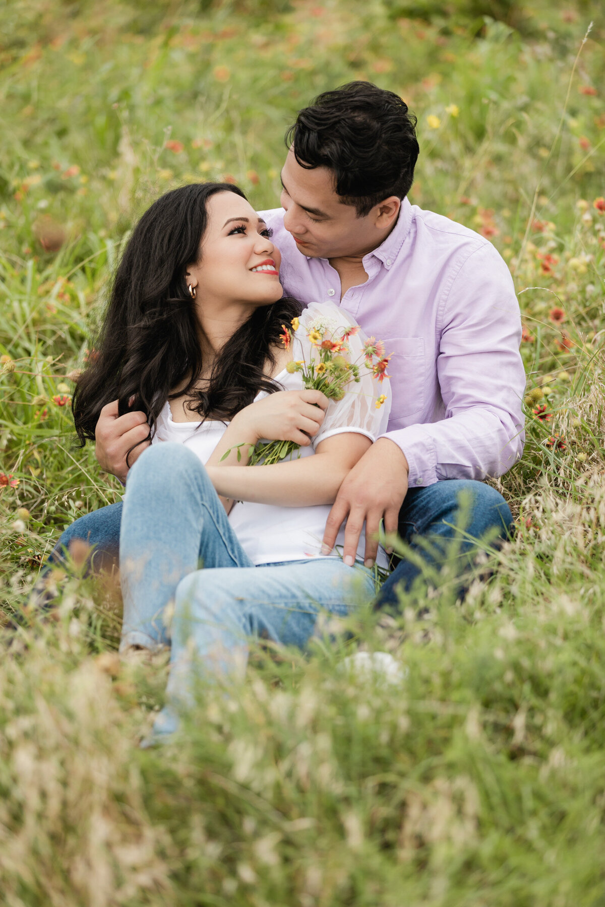 Engaged couple seated in a field of wildflowers at White Rock Lake in Dallas, gazing at each other