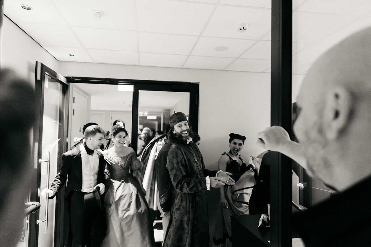 Backstage beeld van allerlei lachende acteurs en performers onderweg naar hun kleedkamer.
