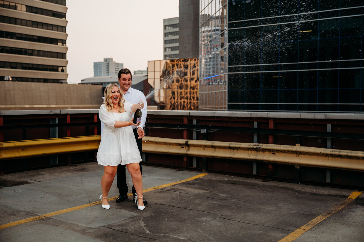 Engaged couple pop a bottle of champagne and celebrate