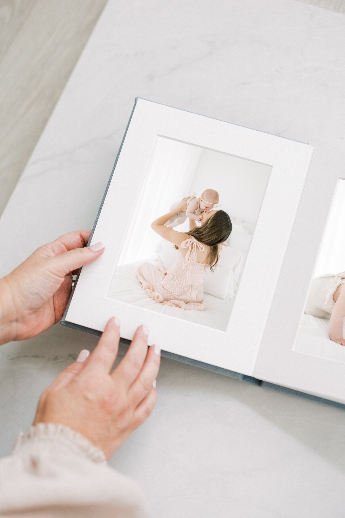 Hands holding matted folio album with printed images from mommy and me session with 6 month old baby