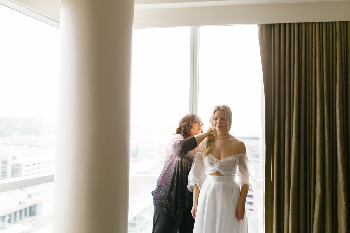 Mom putting necklace on bride in hotel room in Seattle.