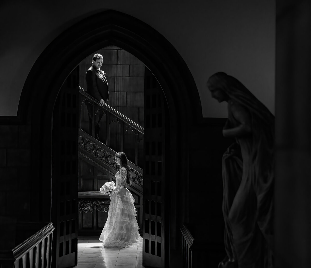A groom looks down at his bride from the ornate wooden steps at Amasa Stone Chapel.