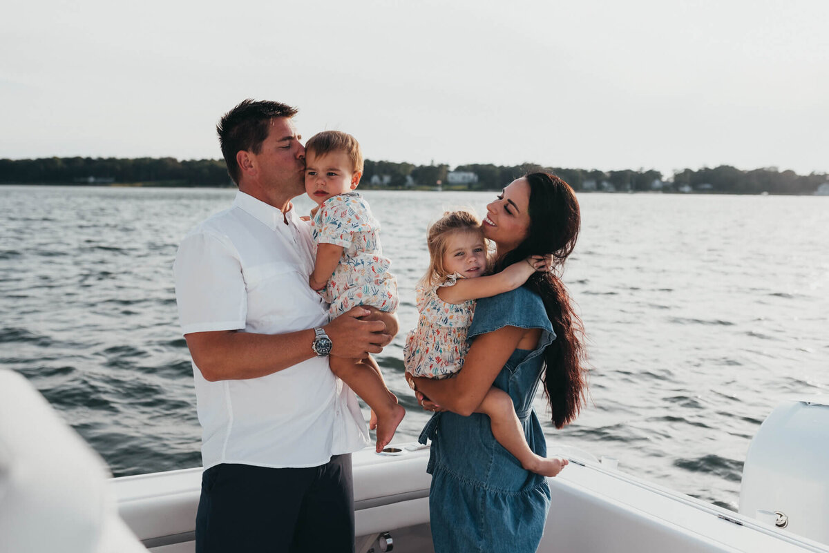 A mother and father hold their two young children on their boat at sunset during their photoshoot with Allison Wolf, Boston Family Photographer