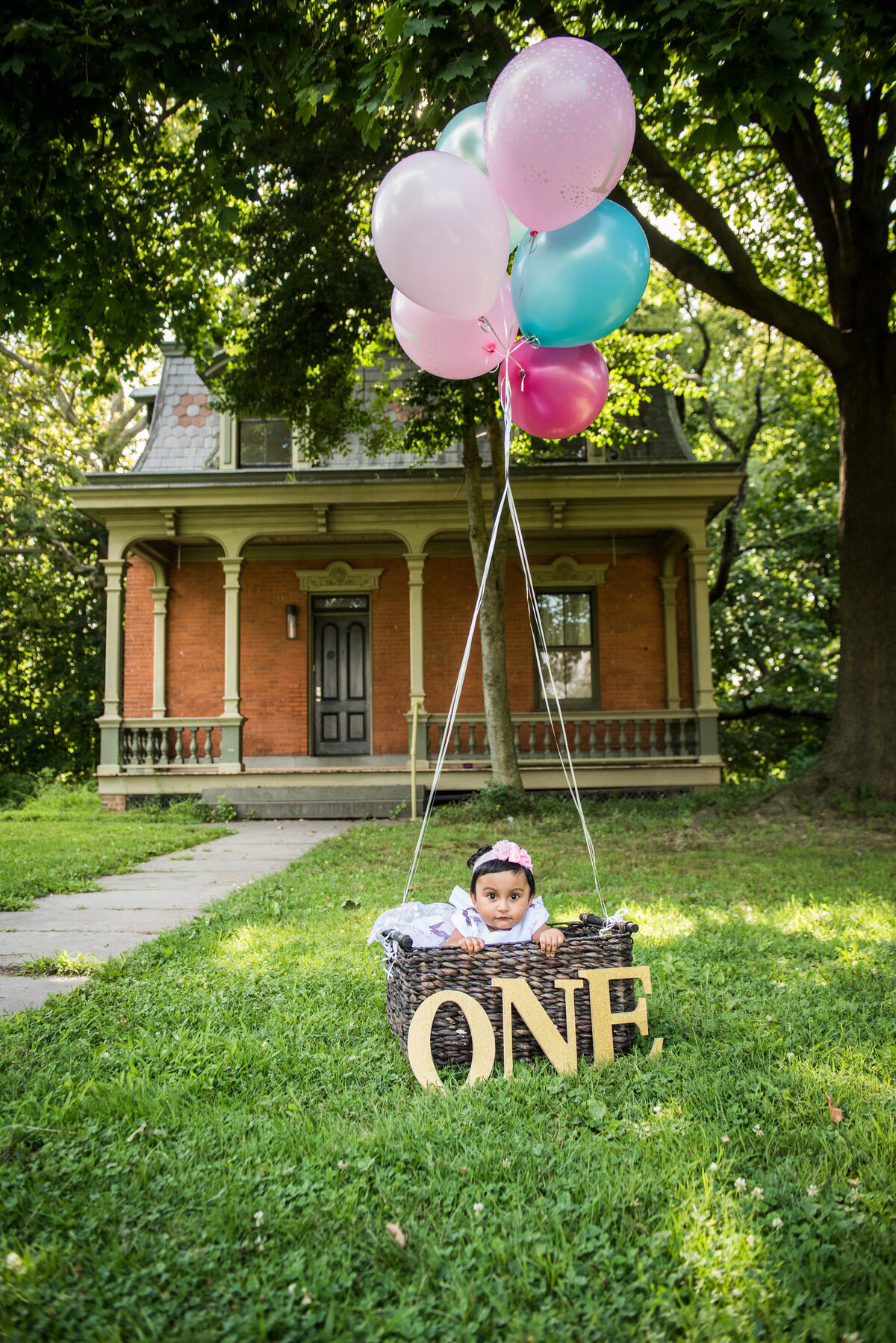 A baby sitting in a basket that says "one" with balloons above them