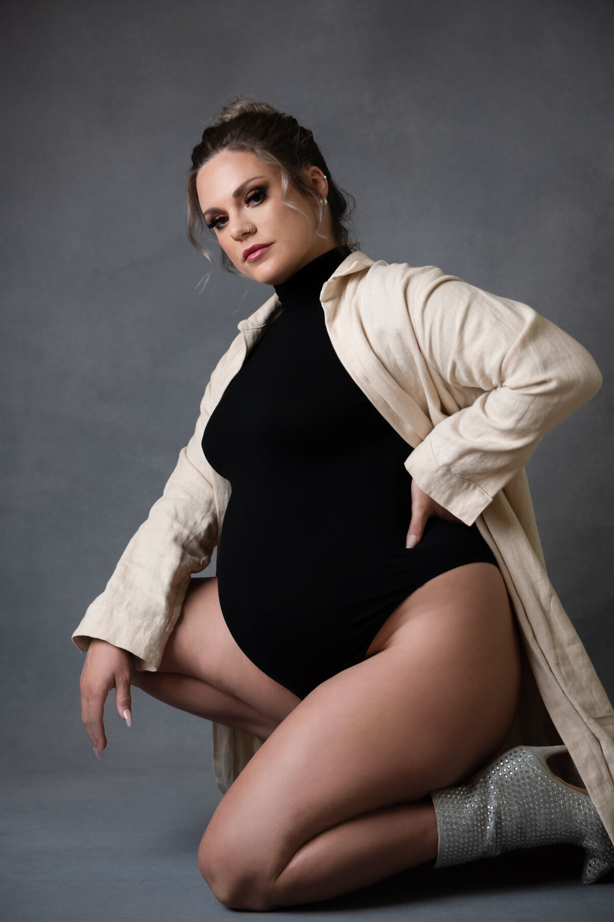 Portrait of a woman in a black bodysuit and cream linen robe, kneeling confidently on one knee. She pair the look with sparkling silver ankle boots.