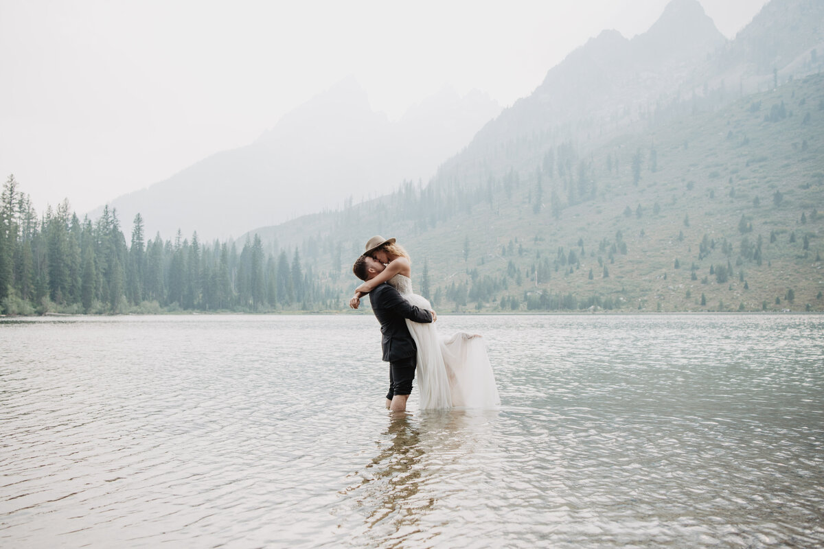 Jackson Hole Photographers capture groom lifting bride during water portraits