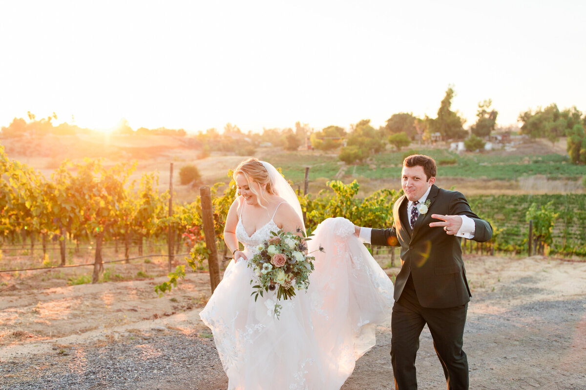 groom holds brides dress as they walk